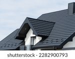 A beautiful modern house is covered with black metal tiles. Roofing of metal profile wavy shape.