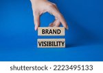 Small photo of Brand visibility symbol. Wooden blocks with words Brand visibility. Beautiful blue background. Businessman hand. Business and Brand visibility concept. Copy space.