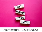 Small photo of You deserve to be well symbol. Wooden blocks with words You deserve to be well. Beautiful red background. You deserve to be well concept. Copy space.