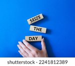 Small photo of Seize the day symbol. Wooden blocks with words Seize the day. Businessman hand. Beautiful blue background. Business and Seize the day concept. Copy space.
