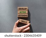 Small photo of Listening skills symbol. Concept word Develop active listening skills on wooden blocks. Beautiful grey background. Businessman hand. Business and Develop active listening skills concept. Copy space