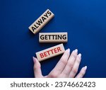Always getting better symbol. Wooden blocks with words Always getting better. Beautiful deep blue background. Businessman hand. Business and Always getting better concept. Copy space.