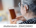 Small photo of Hearing impaired mature woman adjusts settings for her hearing aid via smartphone. Hearing aids, deafness treatment, innovative technologies at audiology