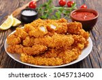 close-up of delicious crispy fried chicken breast strips on white plate, on old rustic  wooden table with tomato sauce and lemon slices, easy recipe for outdoor picnic or party, view from above