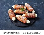 Hungarian kurtos kalacs or chimney cake filled with buttercream decorated with fresh mint on top served on a black serving tray on a dark concrete background, close-up