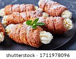 Hungarian street food kurtos kalacs or chimney cake filled with cream decorated with fresh mint on top served on a black plate on a dark concrete background, horizontal orientation, close-up