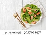 salmon spinach avocado and green pepper salad on a white plate with golden fork and knife on a white wood table, mediterranean healthy diet, horizontal view from above, flat lay, free space