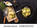 Small photo of Welsh Anglesey Eggs, soft mashed potatoes with hard-boiled eggs all smothered in thick creamy leek and cheese sauce in black bowl on dark table with ingredients, flat lay