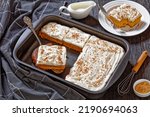 pumpkin cake with cream frosting in baking pan and one slice on a white plate, horizontal view from above