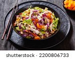 Chinese Chicken Salad with shredded chicken meat, mandarin oranges, crunchy noodles, red cabbage, napa cabbage, carrots, green onions in bowl