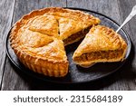 sliced Ground Beef Meat Pie with a flaky puff pastry double crust with hearty minced beef cooked with vegetables and seasoning on black plate on wood table, close-up