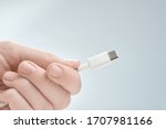 Fingers holding white type-c cable connector on a gray background.