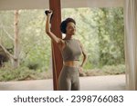 Smiling woman in sportswear exercising with resistance band standing on yoga mat at home