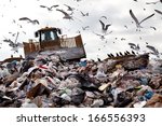 Bulldozer working on landfill with birds in the sky