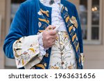 Small photo of The details of man dressed in a baroque costume. A hand holding a pipe, golden buttons, vest and decorative hems.