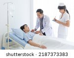 Small photo of Senior doctor and young male patient who lie on the bed while checking pulse, consult and explain with nurse taking note and supporting in hospital wards.