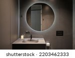 Illuminated round mirror in a dark bathroom interior