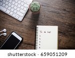 To do list by priority in note book beside are smart phone,keyboard,cactus and small talk on wooden table, business concept