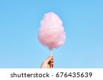 The hands of women holding pink cotton candy in the background of the blue sky