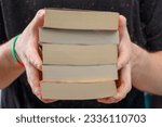 A stack of paperback books held in hands