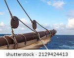 Small photo of Part of the mizzen mast of an old wooden ship, with a sail folded on it, wooden pulleys and ropes against the background of the sea and sky.