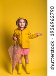 Small photo of Funny kid portrait against yellow background. Kid girl is wearing yellow waterproof raincoat and rubber boots. Weather forecast concept. Child with yellow rain slicker and carrying a pink umbrella