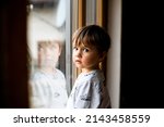 Small photo of Sad kid looking out the window. Reflection in window glass. Face of two years old boy. Alone child. Little migrant child cry. Portrait of kid. Evacuation children. War Ukraine. Refugee abroad.