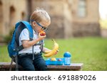Cute schoolboy eating outdoors the school from plastick lunch boxe. Healthy school breakfast for child. Food for lunch, lunchboxes with sandwiches, fruits, vegetables, and water. 