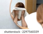 Young woman wiping her face with towel in front of the mirror in the bathroom