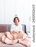 Small photo of Young attractive woman waking up in the bedroom thanks to alarm clock. Discontented girl lying in the bed and holding ringer