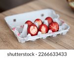 Small photo of Decorated easter eggs in egg box. Red easter eggs in egg carton. Easter eggs decorated with leaves. Interesting method for decorating easter eggs.