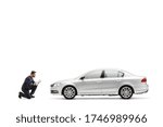 Auto mechanic kneeling in front of a silver car and writing a document isolated on white background