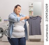 Small photo of Sad woman looking at a shrunken shirt inside a bathroom