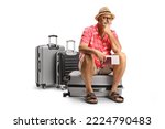 Small photo of Mature male toruist sitting on a suitcase and waiting for a delayed flight isolated on white background