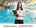 Small photo of Female swimming coach with a whistle holding a clipboard and posing on an indoors swimming pool