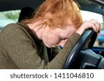 Small photo of Tired-looking young woman with head against the steering wheel of a car