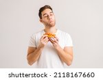 Portrait of satisfied young man with enjoying eating delicious slice of pizza, with closed eyes from pleasure on white isolated background. Studio shot of hungry male student eating tasty food.