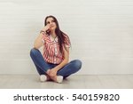 Dreaming woman sitting on the floor of her room background, isolated white bricks wall. Young pretty female thinking of furnishing her new apartment.