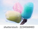Three bags of cotton candy in three colors. Hold in hand on sky background. Cotton candy made from sugar spun into thin noodles. Like a cloud, many colors depending on the color                 