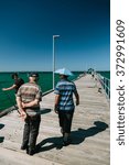 Small photo of MELBOURNE/AUSTRALIA - FEBRUARY 6: Locals fishing on the jetty in Mordialloc, a coastal suburb of Melbourne, Australia. In the foreground a man walks with his friend who wears an umbrella for a hat.