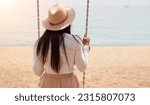 Small photo of Photo of a unrecognizable woman sitting in a swinger outdoors in the beach. Female traveler enjoying the good time in summer. Copy space.