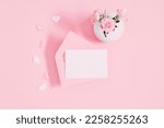 Top view on open pink envelope with paper card, bouquet of pink rose  flowers in vase and heart confetti on pastel pink table background. Birthday, Wedding, Mother's Day, Valentine's day, Women's Day.