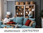 Small photo of Simple living. Happy middle-aged senior couple 70s husband and wife sit relax on couch in living room reading book drinking tea together, calm elderly 60s couple booklovers rest at home enjoy life