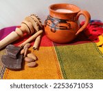 Small photo of Mexican hot chocolate on traditional mug, chocolate pieces, cinnamon sticks and wooden skimmer on colorful tablecloth