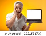 Small photo of Surprised excited man with beardless white hair pointing at blank laptop screen, looking at camera with big eyes, shocked by advertisement. Indoor studio shot isolated on yellow background