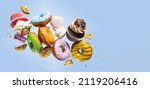 Small photo of Colorful decorated donuts, cupcakes and macaroons falling in motion on blue background with sprinkling. Sweet and various doughnuts flying on pastel backdrop. Banner