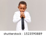 Small photo of Portrait of nervous frustrated sad African American schoolboy in uniform looking down with worried facial expression, gnawing nails, scared of being told off for bad marks at school. Sincere emotions