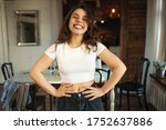 Leisure, relaxation, home and domesticity. Positive cheerful teenage girl wearing crop top smiling broadly at camera, having fun indoors, spending day at home, keeping hands on her waist, laughing