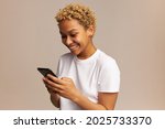 Communicating woman with Afro hairstyle using mobile phone, posing against wall with copy space for advertising content, having happy, cheerful look, reading funny message from her friend