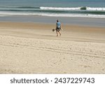 Small photo of St Augustine, Florida — March 2, 2023: Solitary beachcomber walks at high tide mark of sand beach in Florida